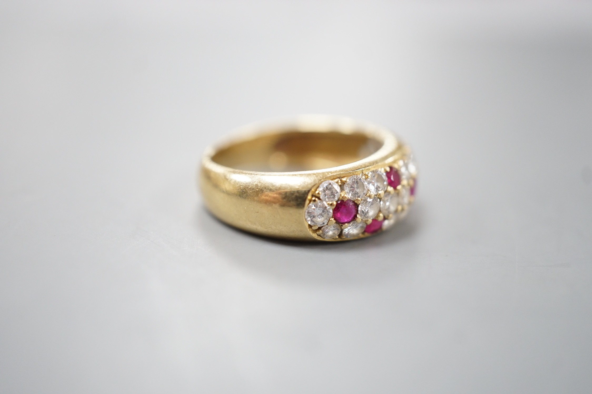A modern yellow metal, ruby and diamond cluster set half hoop ring, size L/M, gross weight 4.5 grams.